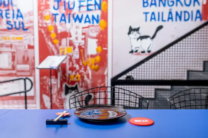 Mesa azul diante do mural de vielas asiáticas com o gato e a escada